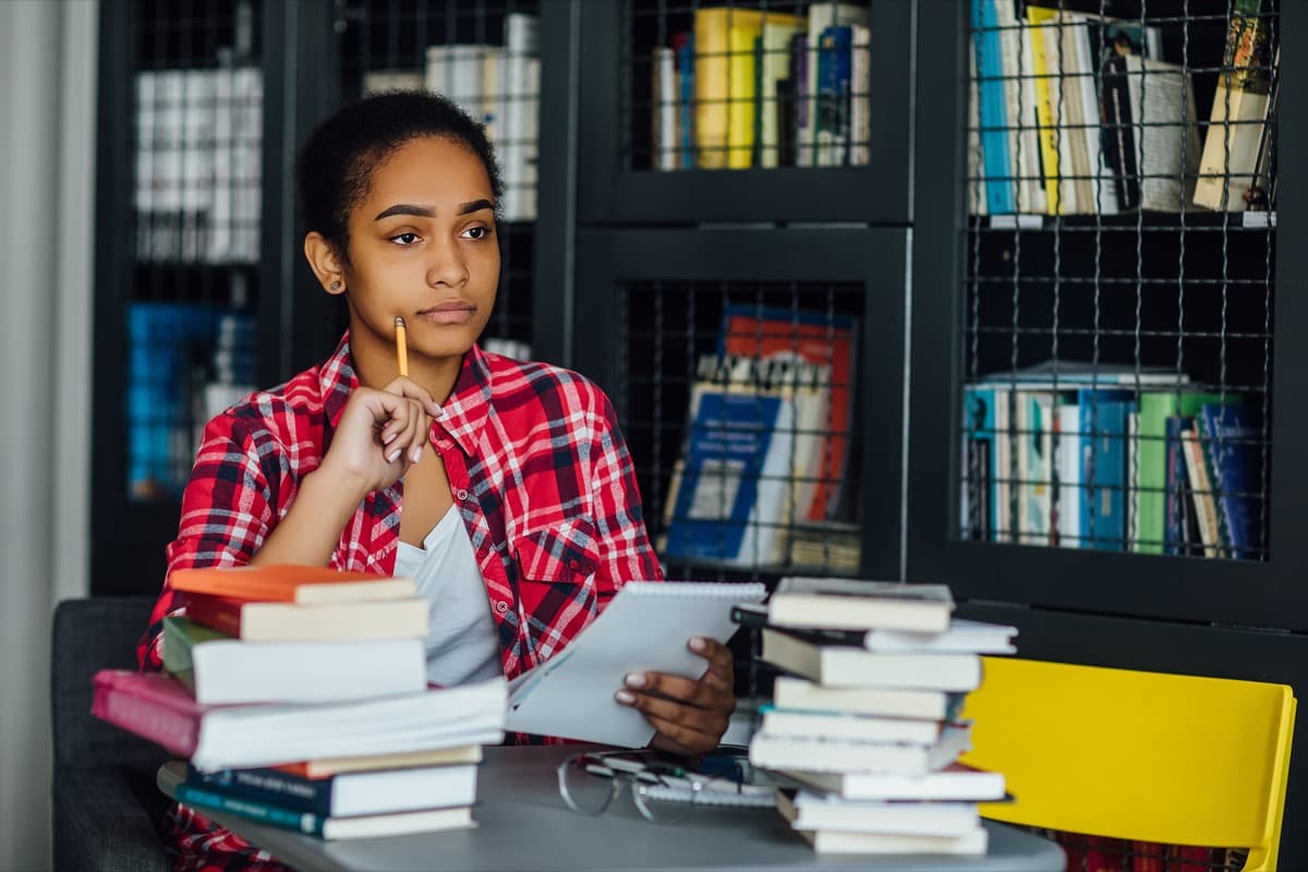 A student studying at a desk stacked with books